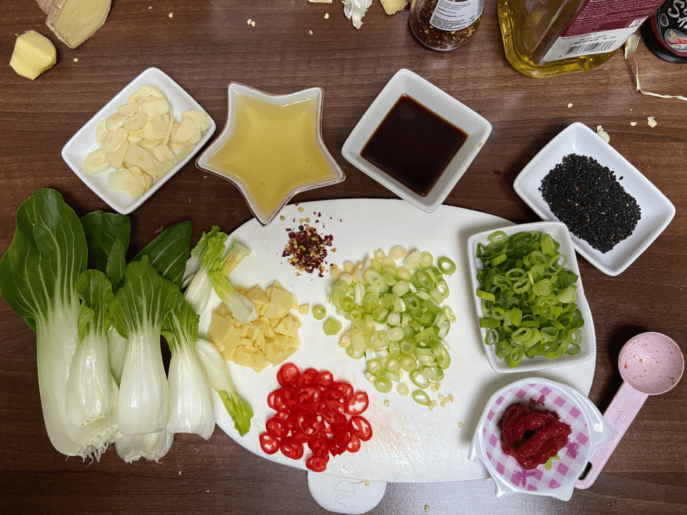 Preparation for vegetarian ramen noodles broth with sliced garlic, vegetable oil, soya sauce, scallions, tomato pure, pok choy, sliced chili pepper, sliced ginger, black sesame seeds